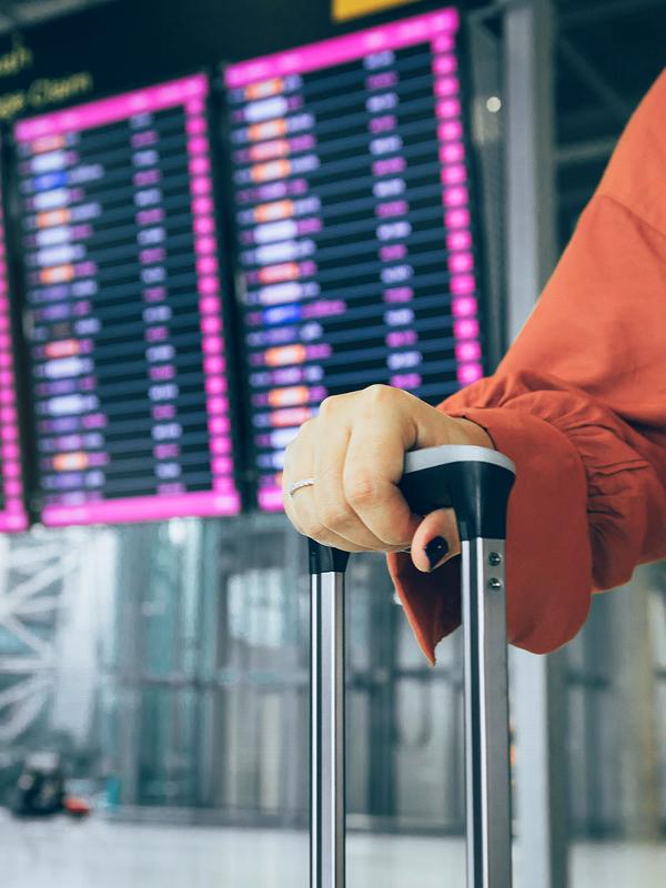 Landy holding luggage Infront of checking boards at airport